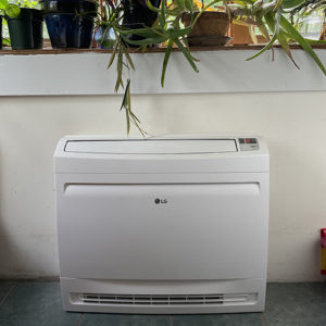 A rectangular white indoor floor heat exchanger for a cold climate air source heat pump, with plants on a shelf above it.